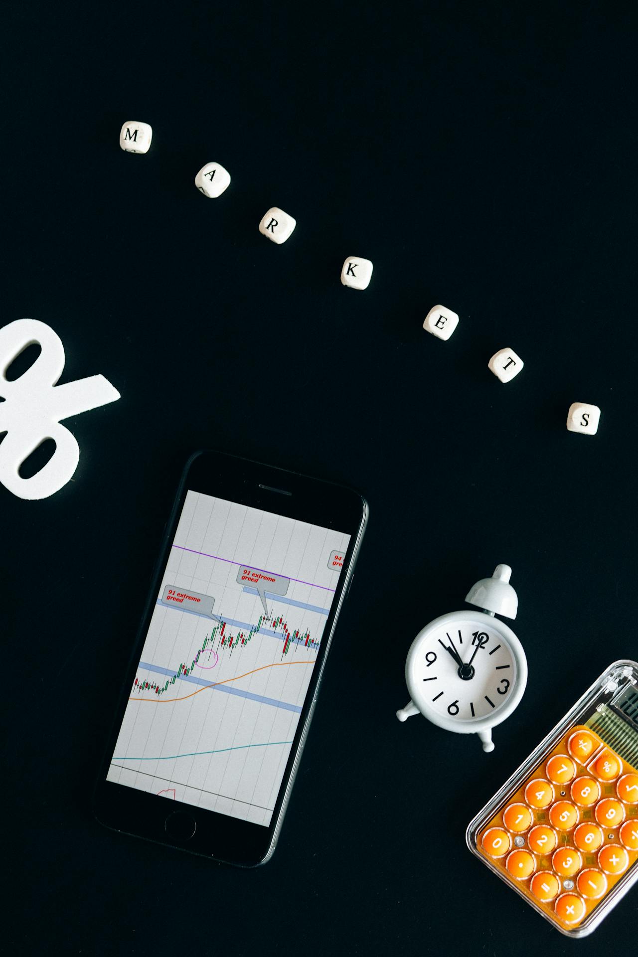 Smartfon z wykresem giełdowym, obok zegar, kalkulator i napis „Markets” z kostek (kobalt)